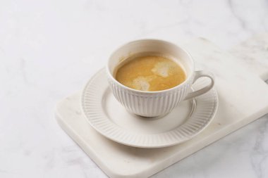 Beyaz bir masada mermer bir tahtada sütlü beyaz porselen bir fincan.