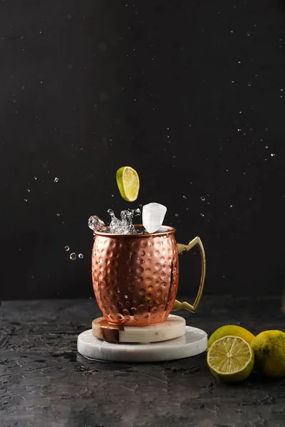 白い大理石の板の上にレモンと氷のキューブを飛んで銅マグカップで伝統的なアメリカのアルコール飲料モスクワラバ 黒の背景 — ストック写真