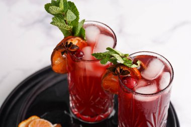 cTraditional christmas beverage mulled wine with red cherry juice, orange tangerines, cinnamon sticks, ice cubes and anise on black trays