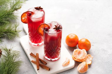 Geleneksel noel içeceği kırmızı kiraz suyu, portakal mandalinası, tarçın çubuğu, buz küpleri ve mermer bir tahtanın üzerinde anason.