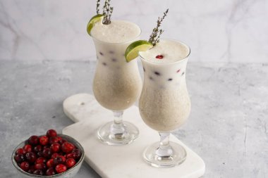 Uzun kokteyl bardakları, muzlu milkshake, kızılcık ve hindistan cevizi beyaz mermer tahtada.