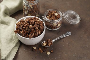 Kahvaltı müsli gevreği. Çikolata parçacıklı ve fındıklı. Birkaç kavanoz ve kâse, süt şişesi, kahverengi ahşap yüzey.