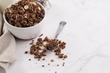 Kahvaltı müsli gevreği. Çikolata parçalı ve fındıklı. Birkaç kavanoz ve kâse, süt şişesi, beyaz yüzey.