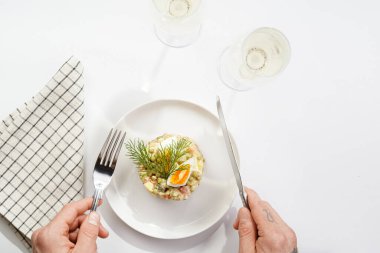 Male hand holding silver fork and knife over a traditional east european dish for New Year's Eve - salad 