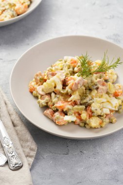 Yeni yıl arifesi için geleneksel Doğu Avrupa yemeği - patates, havuç, soğan, bezelye, sosis, salatalık, yumurta ve mayonez salatası ve gri bir kasede 