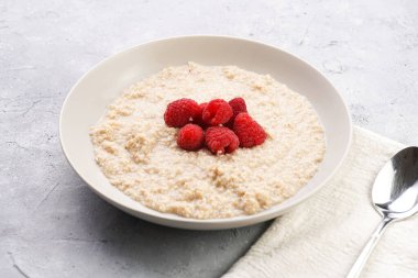 Kahvaltı kasesi, yulaf lapası ve gri yüzeyde taze ahududu.