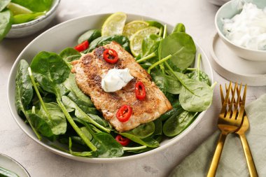 Taze çiğ ıspanak ve kızarmış yabani somon, limon dilimleri, krem peynir sosu, gri beton yüzeyde kırmızı biber.