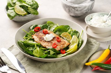 Taze çiğ ıspanak ve kızarmış yabani somon, limon dilimleri, krem peynir sosu, gri beton yüzeyde kırmızı biber.