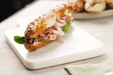 Yulaf ezmeli, domuz dilimli prosciutto, sert peynirli gouda ve mermer tahtada taze yeşillik, bej yüzeyle süslenmiş kahverengi küllü ekmek çubuklarıyla uzun sandviç.