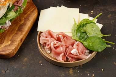 Yulaf ezmesi, domuz dilimleri prosciutto, sert peynirli gouda ve ahşap tahtalarda taze yeşillikler ile süslenmiş kahverengi küllü ekmek çubuklarıyla uzun sandviç.