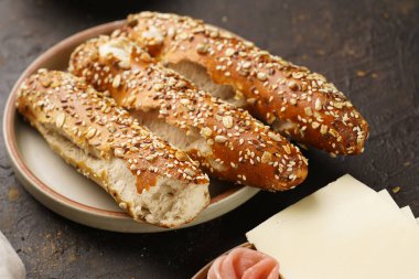 Lezzetli kahvaltı malzemeleri: yulaf, domuz dilimleri prosciutto, sert peynirli gouda ve ahşap tahtalarda taze yeşillikler ile süslenmiş kahverengi küllü ekmek çubukları.