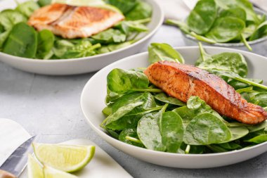 Taze çiğ ıspanak ve kızarmış kırmızı somon ile gri beton yüzeyde limon dilimleri.