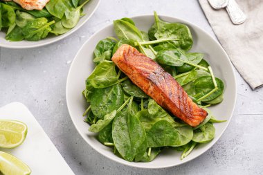 Taze çiğ ıspanak ve kızarmış kırmızı somon ile gri beton yüzeyde limon dilimleri.