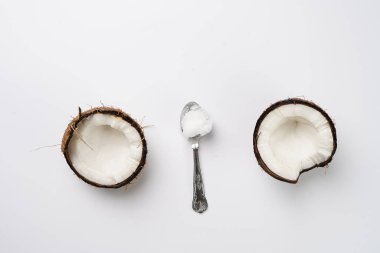 Kırılmış hindistan cevizi ve beyaz bir yüzey üzerinde hindistan cevizi yağı ile çay kaşığı.