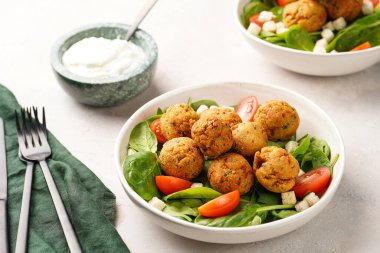 Nohut köfteli salata kasesi taze yeşil ıspanak, kiraz domatesleri, kızarmış ekmek ve gri bir taş yüzeyde naneli yoğurt sosu.