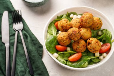 Nohut köfteli salata kasesi taze yeşil ıspanak, kiraz domatesleri, kızarmış ekmek ve gri bir taş yüzeyde naneli yoğurt sosu.