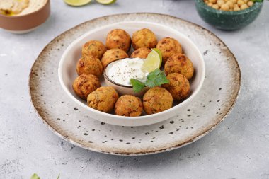 Geleneksel oryantal nohut bol yağda kızartılmış falafel tzatziki yoğurt sosu, humus, taze limon ve açık gri beton yüzeyde yeşil kişniş.