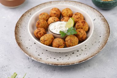 Geleneksel oryantal nohut bol yağda kızartılmış falafel tzatziki yoğurt sosu, humus, taze limon ve açık gri beton yüzeyde yeşil kişniş.