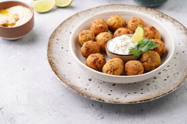 Geleneksel oryantal nohut bol yağda kızartılmış falafel tzatziki yoğurt sosu, humus, taze limon ve açık gri beton yüzeyde yeşil kişniş.