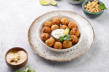 Geleneksel oryantal nohut bol yağda kızartılmış falafel tzatziki yoğurt sosu, humus, taze limon ve açık gri beton yüzeyde yeşil kişniş.