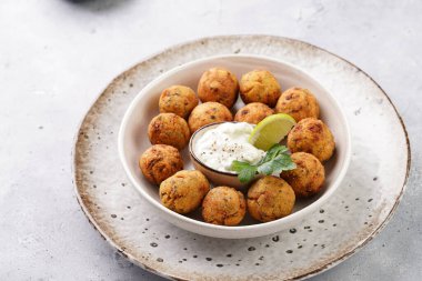 Geleneksel oryantal nohut bol yağda kızartılmış falafel tzatziki yoğurt sosu, humus, taze limon ve açık gri beton yüzeyde yeşil kişniş.