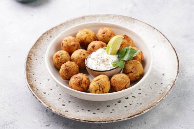 Geleneksel oryantal nohut bol yağda kızartılmış falafel tzatziki yoğurt sosu, humus, taze limon ve açık gri beton yüzeyde yeşil kişniş.