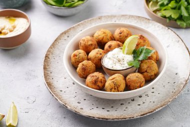 Geleneksel oryantal nohut bol yağda kızartılmış falafel tzatziki yoğurt sosu, humus, taze limon ve açık gri beton yüzeyde yeşil kişniş.