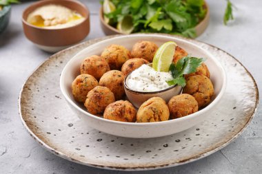 Geleneksel oryantal nohut bol yağda kızartılmış falafel tzatziki yoğurt sosu, humus, taze limon ve açık gri beton yüzeyde yeşil kişniş.