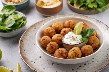 Geleneksel oryantal nohut bol yağda kızartılmış falafel tzatziki yoğurt sosu, humus, taze limon ve açık gri beton yüzeyde yeşil kişniş.