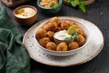 Geleneksel oryantal nohut bol yağda kızartılmış falafel tzatziki yoğurt sosu, humus taze limon ve siyah yüzeye yeşil kişniş.