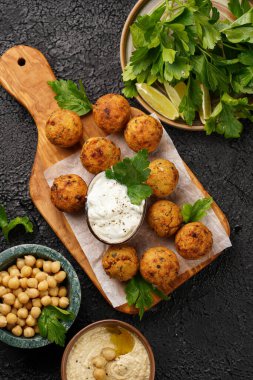 Geleneksel oryantal nohut, ahşap bir tahtada kızartılmış falafel, tzatziki yoğurt sosu, humus, taze limon ve siyah yüzeyde yeşil kişniş.