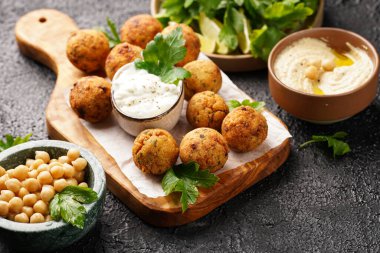 Geleneksel oryantal nohut, ahşap bir tahtada kızartılmış falafel, tzatziki yoğurt sosu, humus, taze limon ve siyah yüzeyde yeşil kişniş.