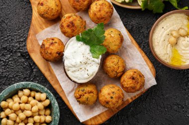 Geleneksel oryantal nohut, ahşap bir tahtada kızartılmış falafel, tzatziki yoğurt sosu, humus, limon ve siyah yüzeyde taze yeşil kişniş.