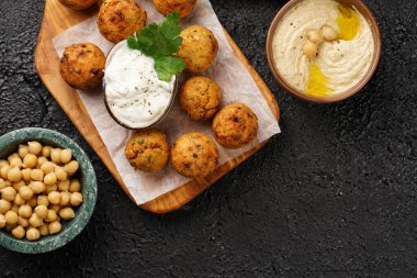 Geleneksel oryantal nohut, ahşap bir tahtada kızartılmış falafel, tzatziki yoğurt sosu, humus, taze limon ve yeşil kişniş, siyah yüzey üzerinde kopyalama alanı.