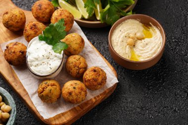 Geleneksel oryantal nohut, ahşap bir tahtada kızartılmış falafel, tzatziki yoğurt sosu, humus, taze limon ve siyah yüzeyde yeşil kişniş.