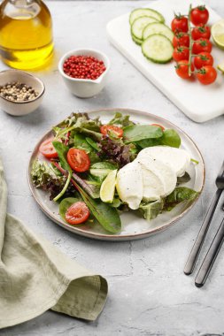 Yeşil yapraklı salata, marul, ıspanak, kiraz domatesleri, mozarella, zeytinyağı, biber, gri taş yüzeyde limon suyu.