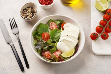 Yeşil yapraklı salata, marul, ıspanak, kiraz domatesleri, mozarella, zeytinyağı, biber, gri taş yüzeyde limon suyu.