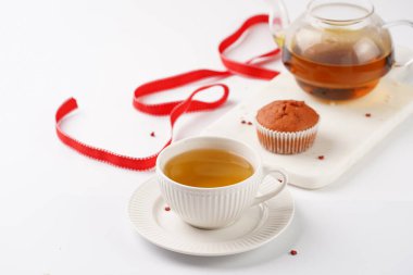 Beyaz yüzeydeki mermer tahtada birkaç ev yapımı beyaz ve pembe kek, kırmızı kurdele, kalp şeklinde kırmızı ve beyaz şeker süslemesi ve çay demliği.