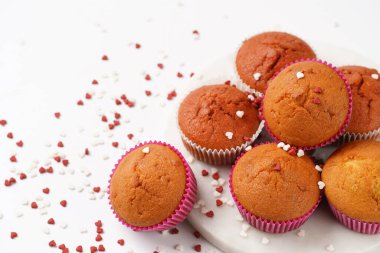 Beyaz yüzeydeki mermer tahtada, kalp şeklinde kırmızı ve beyaz şeker süslemeli ev yapımı beyaz ve pembe kekler.