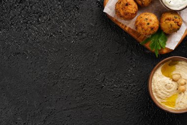 Geleneksel oryantal nohut, ahşap bir tahtada kızartılmış falafel, tzatziki yoğurt sosu, humus, taze limon ve yeşil kişniş, siyah yüzey üzerinde kopyalama alanı.