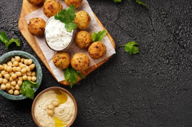 Geleneksel oryantal nohut, ahşap bir tahtada kızartılmış falafel, tzatziki yoğurt sosu, humus, taze limon ve yeşil kişniş, siyah yüzey üzerinde kopyalama alanı.