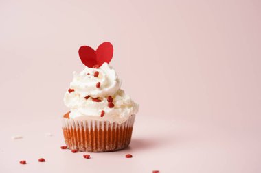 Beyaz kremalı ev yapımı çikolatalı kek ve pembe yüzeydeki mermer tahtada kalp paylaşımı kırmızı ve beyaz şeker süslemesi.