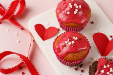 Kırmızı kremalı üç ev yapımı beyaz ve çikolatalı kek ve pembe yüzeydeki mermer tahtada kalp paylaşımı kırmızı ve beyaz şeker süslemesi.