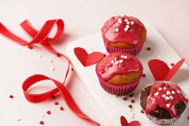 Kırmızı kremalı üç ev yapımı beyaz ve çikolatalı kek ve pembe yüzeydeki mermer tahtada kalp paylaşımı kırmızı ve beyaz şeker süslemesi.