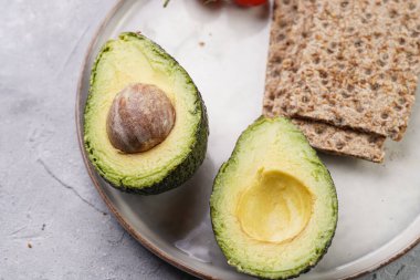 Sağlıklı çıtır çıtır ekmek sandviçi için gerekenler: Avokado, kraker ve yuvarlak tarama tabağında kiraz domatesleri
