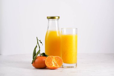 Turuncu mangolu uzun cam, beyaz yüzeyde birkaç mandalina.