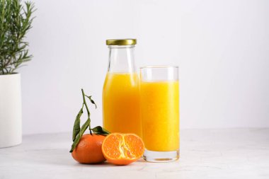 Turuncu mangolu uzun cam, beyaz yüzeyde birkaç mandalina.