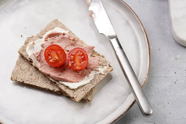 Healthy crunchy crisp bread sandwich with chicken pate, cream cheese and cherry tomatoes on round scandi plate