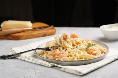 Ağır kremalı makarna ile düz tabak ve sarımsak soslu kızarmış karides ve beton yüzeyde parmesan peyniri.