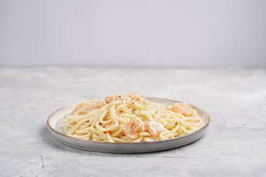 Ağır kremalı makarna ile düz tabak ve sarımsak soslu kızarmış karides ve beton yüzeyde parmesan peyniri.